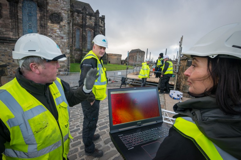 team of people in hi-vis and hard hards around a laptop
