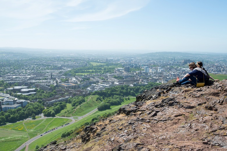 A couple sit and admire the view at the summit of Arthur's Seat, Holyrood Park.