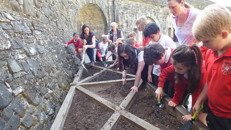 Children in school uniform diffing in a raised flower bed with trowels