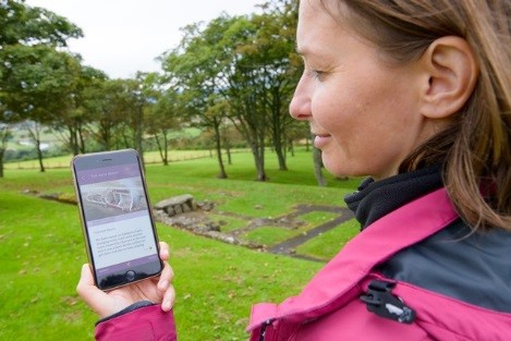 A woman at the site of a Roman fort uses an app on her phone 