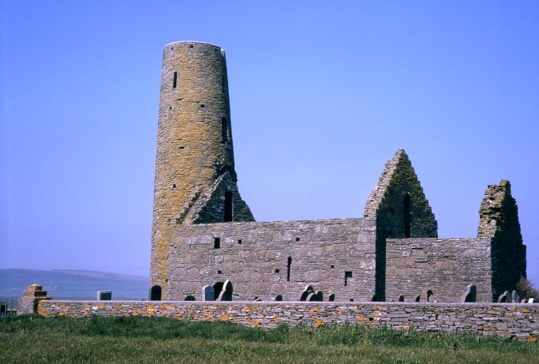 A general view of St Magnus' Church in Orkney. A distinctive round tower is at one end of the church which has no roof. There is a walled graveyard in the foreground. 