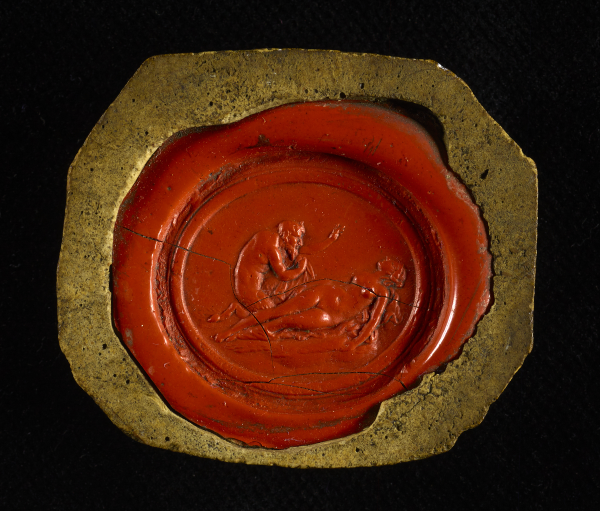 A small red wax seal containing intricate, classical-looking artwork. A nude lady is shown interacting with a bearded man. The man has a tail which suggests this may be a representation of the Devil. 