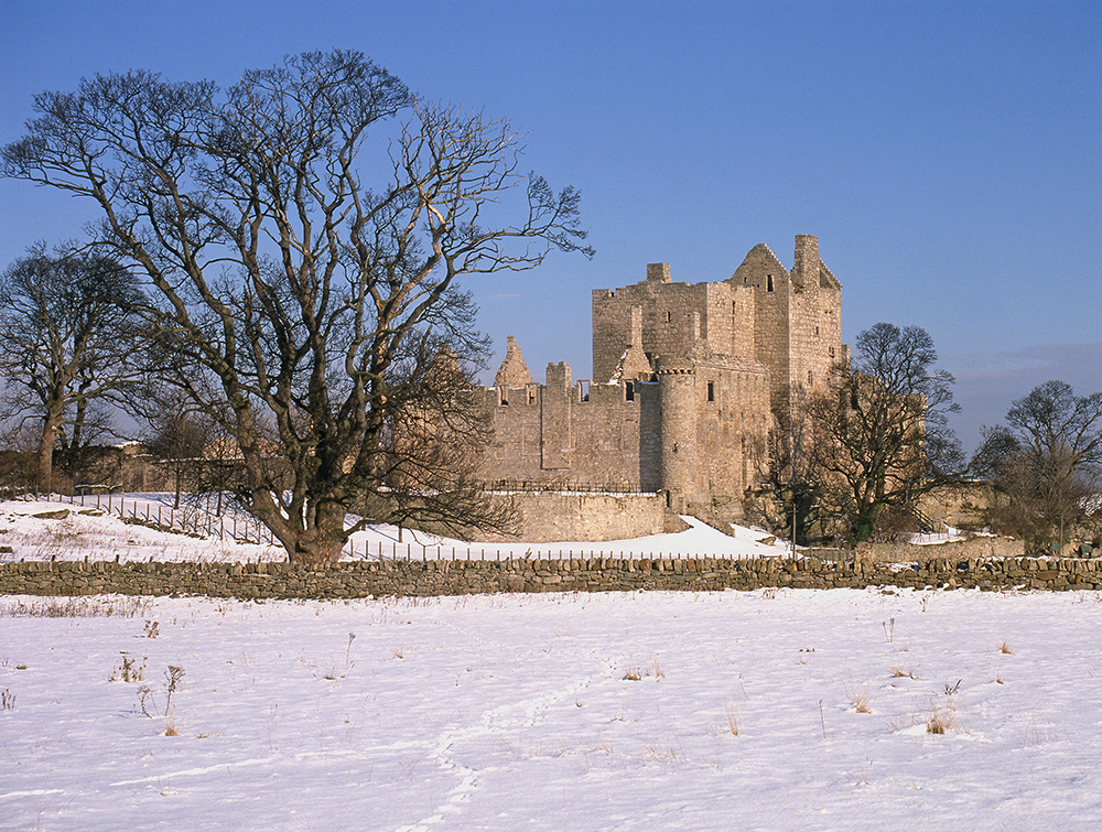 An exterior view of Craigmillar Castle. Snow is on the ground. Some footprints or animal tracks lead through the snow towards the castle. 