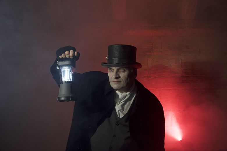 a ghoulish man in Victorian dress and top hat holds up a lantern