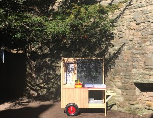 A wooden cart containing art equipment parked under a tree in a castle courtyard