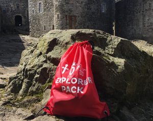 A red drawstring bag labelled Explorer Pack in front of a castle building. 