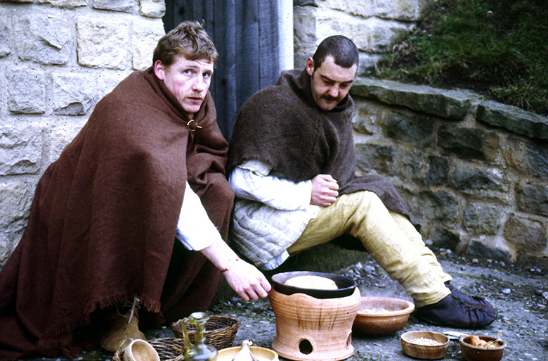 Two members of a Roman history reenactment group cook food over a replica North African style pot. 