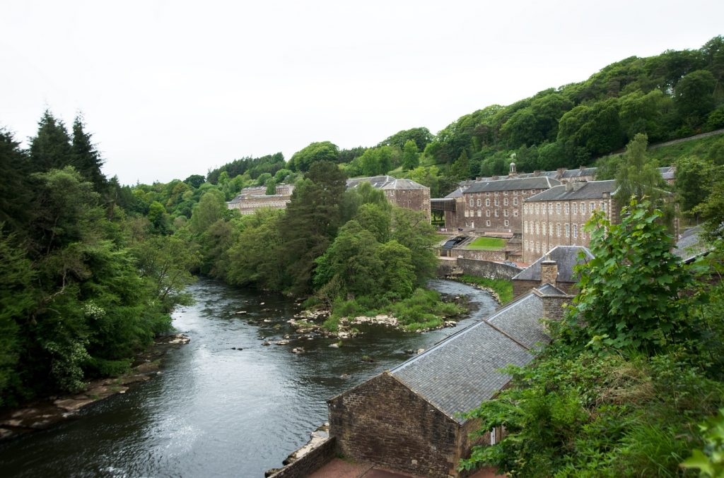 A photograph of industrial mills by a river with trees.