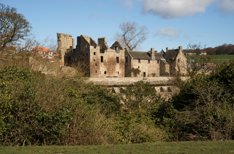 The extensive ruins of Aberdour Castle viewed through green foliage 