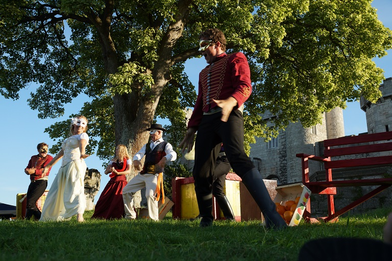 A group of actors perform outside wearing masks