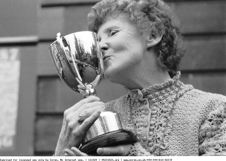 Black and white archive image. A woman holding a trophy and kissing in smiling