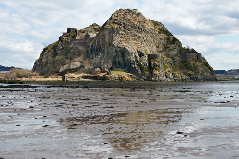 A muddy riverbed in front of a huge rock upon which a castle has been built