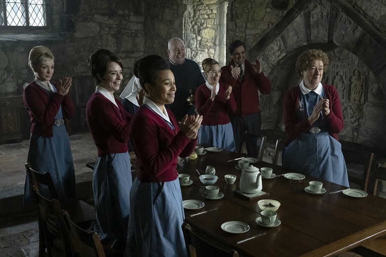 Still from an episode of Call the Midwife showing the cast at a dining table inside a medieval church 