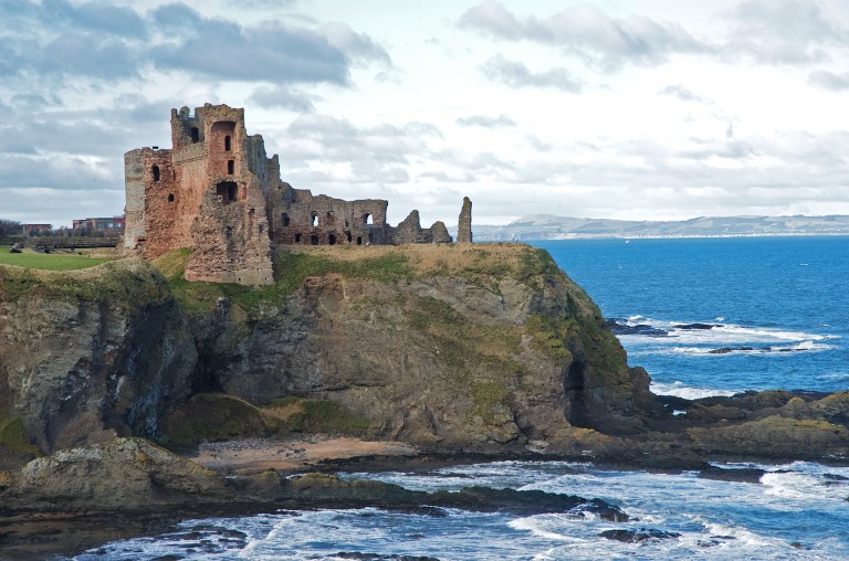 A shot of the ruined Tantallon Castle, showing its dramatic cliff top position. Waves crash on the rocks below the castle. 