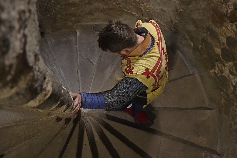 man dressed as Robert the Bruce descends a spiral staircase in a castle