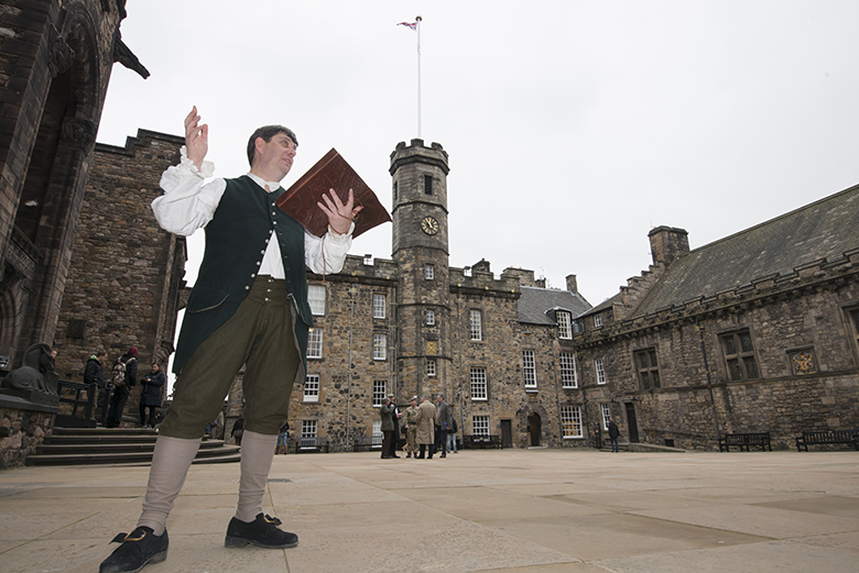 A man dressed as Rabbie Burns stands in front of Edinburgh Castle with a book of poetry in his hand