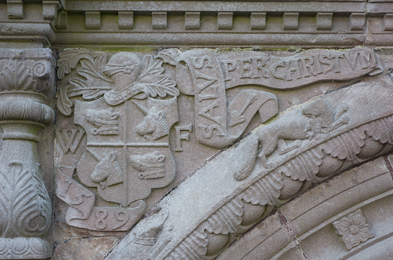 Ornate carving including a coat of arms which has unicorn heads in the top right and bottom left quarters. A boars head is carved in the other two quarters. 