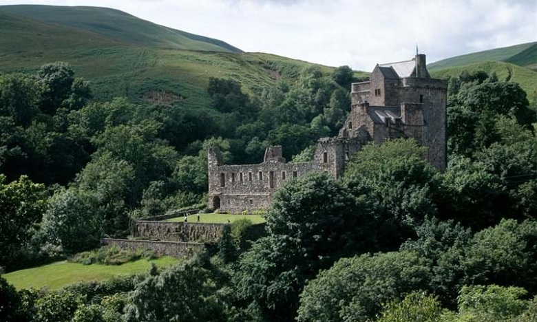A view of Castle Campbell set at the head of luscious green glen. A handful of visitors can be seen exploring the grounds. 