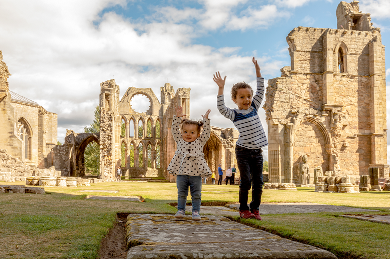 Two children make a pose in front of the ruins of a cathedral