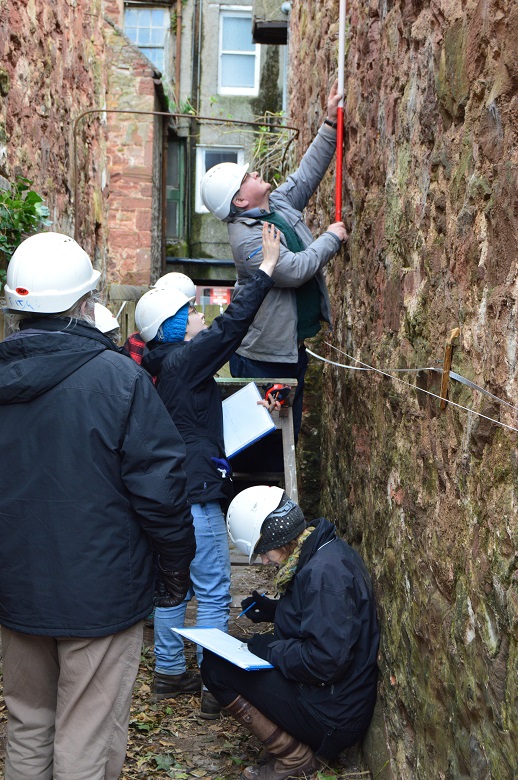 A team in white hard hats workling on a survey of a narrow urban close 