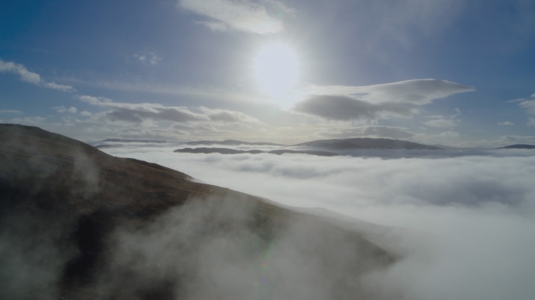 Aerial shot of the sun rising over low-lying clouds and mountain tops