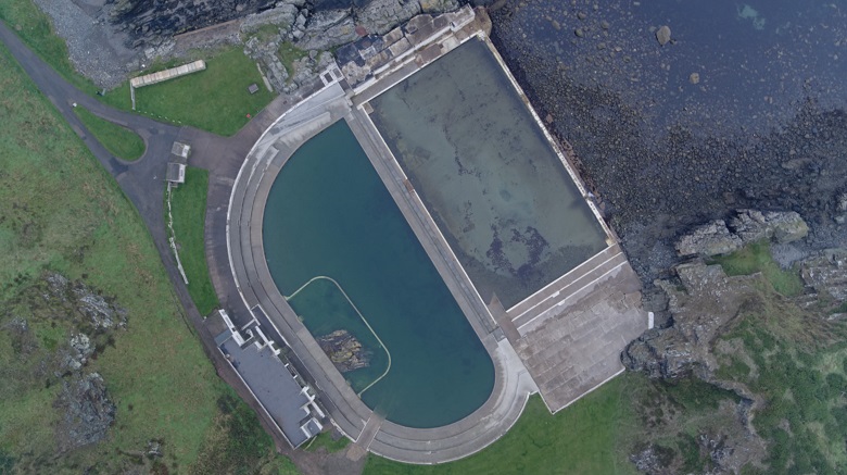Aerial shot of a deserted lido sitting immediately next to a rocky coastline 