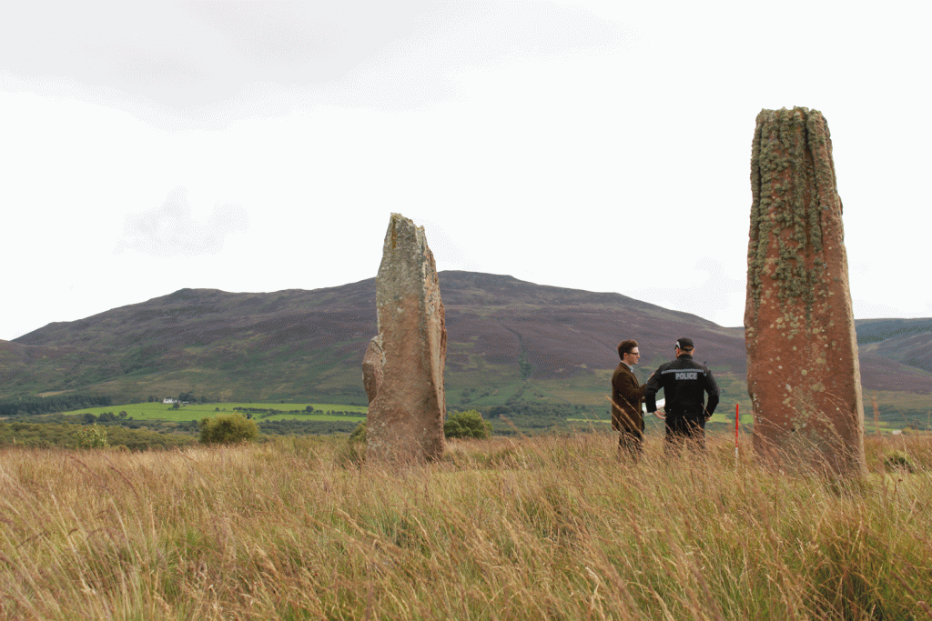 Man and a police officer stand beside tall standing stones.