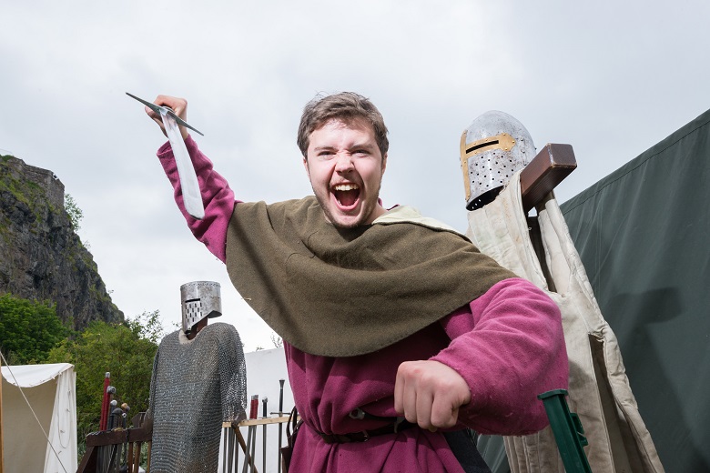 A reenactor in medieval clothing brandishing a sword 