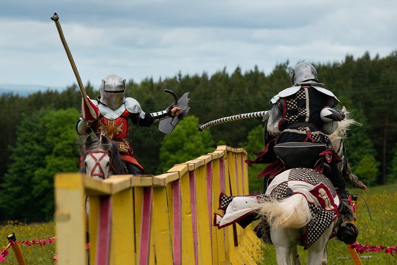 Action shot of two knights on horseback galloping towards each other with raised lances 