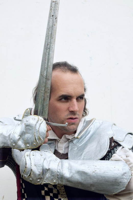 An angry looking knight wearing silver armour and grasping a sword with both hands 