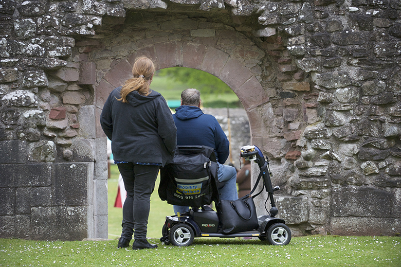 Visitors at Dryburgh Abbey look through an archway. One of the visitors is using a mobility scooter