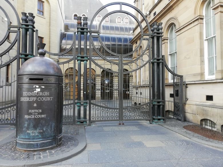 View of the entrance to Edinburgh's Sheriff Court. It is a modern facade with gates and a large post box located outside