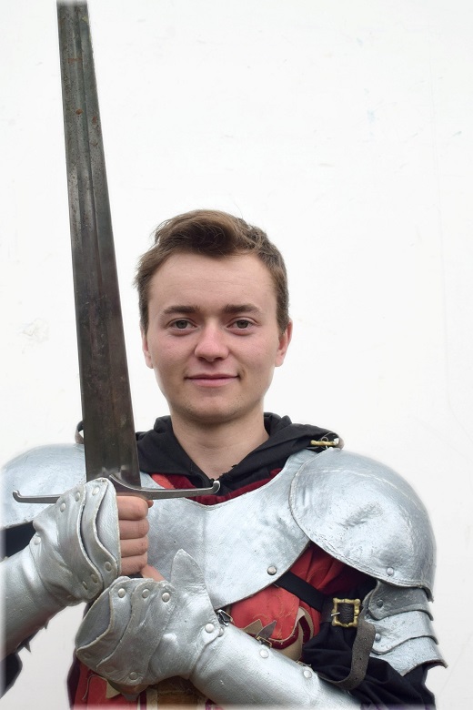 A young man wearing knight's armour posing with a large sword