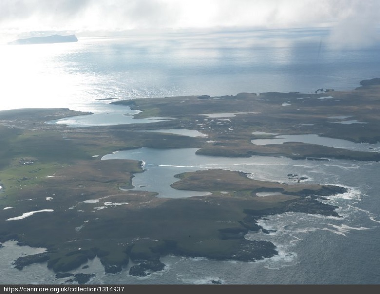 An aerial view of Papa Stour showing numerous bays and inlets, and the sun shining onto the sea in the background