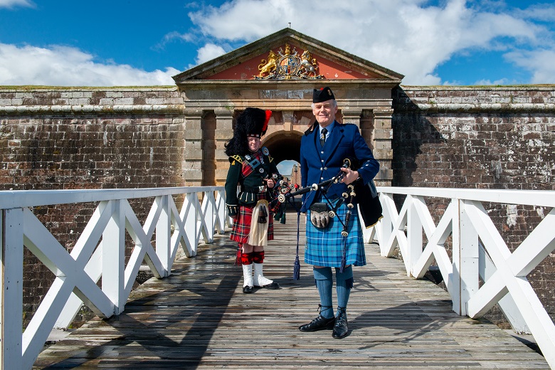 Two pipers in Highland dress pose in front of the entrance to Fort George 