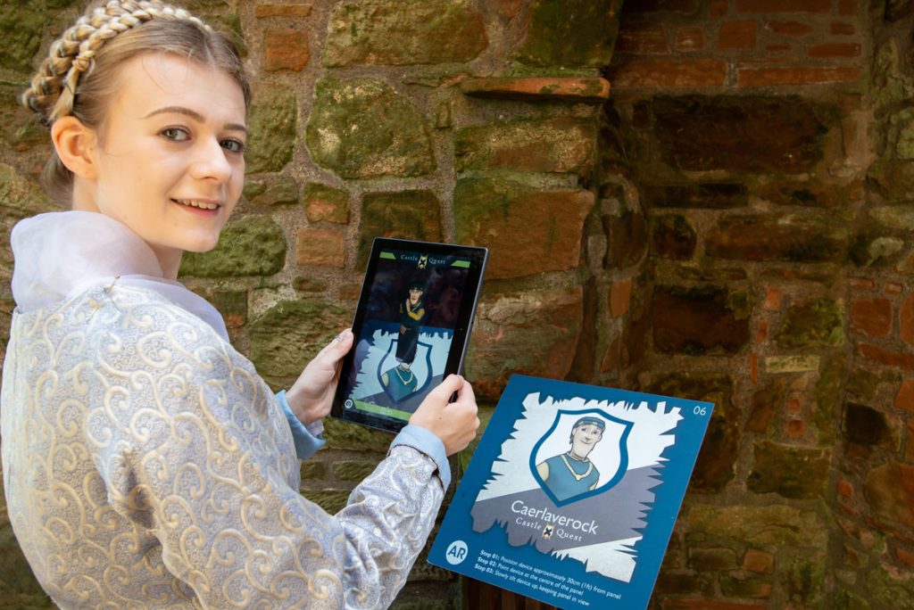 A woman with blonde hair holds up a device towards a sign. A cartoon character has appeared on her device.