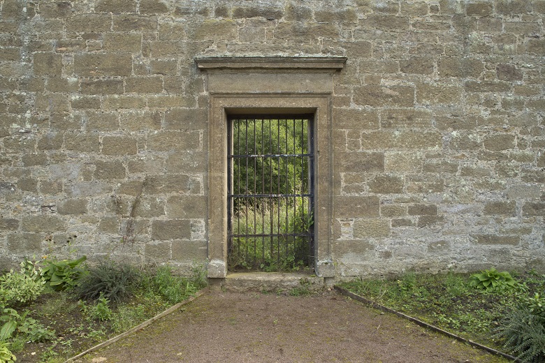 A black metal gate within the wall of a walled garden 