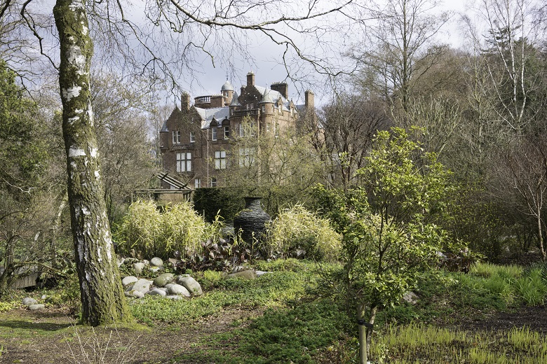 A garden with trees and shrubs, and threave estate buildings in the background