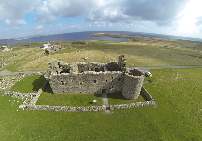 Aerial view of Muness Castle with the seashore in the background