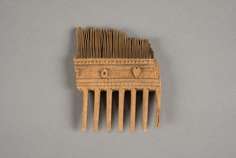 Fragment of a comb which has wide set teeth on one side and fine teeth on the other. In the middle section there are small carvings of a heart and geometric shape.