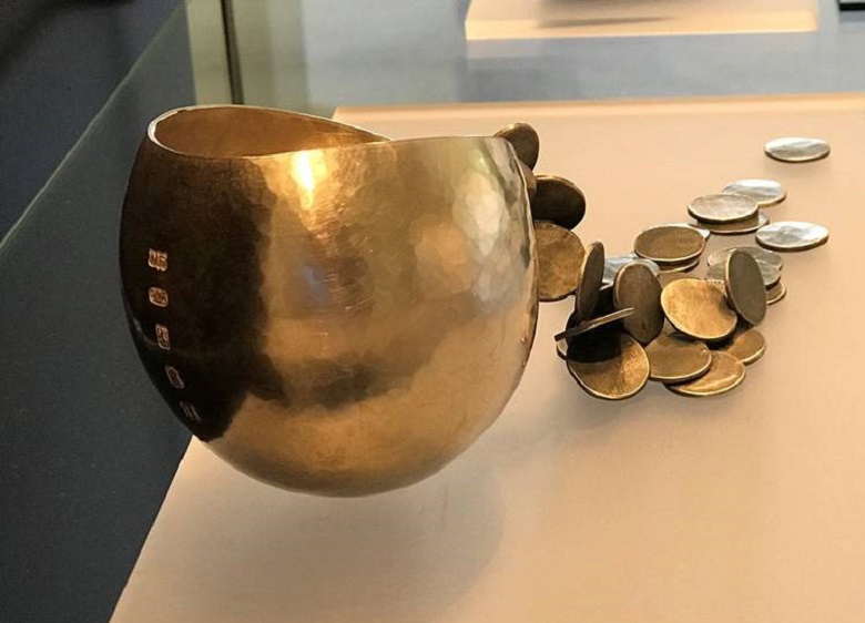 a sculpture. It's made from shiny metal which has been hammered into a cup shape and a number of disks, soldered together, are spilling out of the open cup 