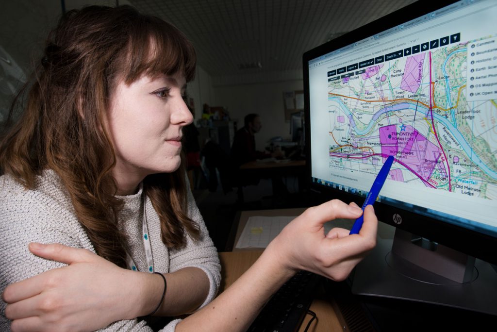A woman with brown hair looks at a computer screen showing a map.