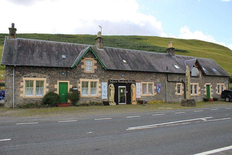 A small row of cottages close to a road. The entrance to an art gallery in the centre of the building is flanked by two sculpted wooden figures 