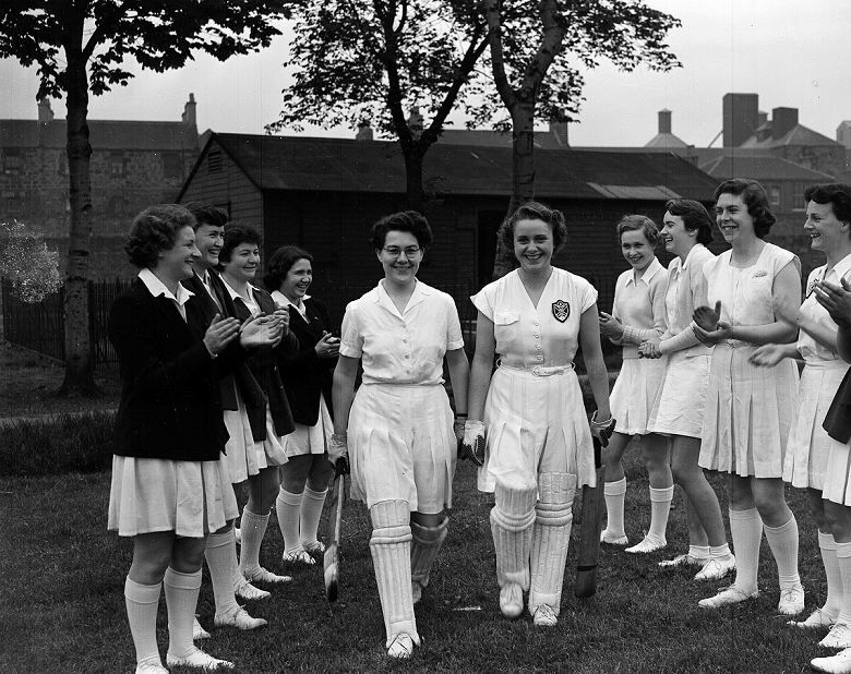 Archive photo of a ladies cricket team. Two players wearing pads and carrying bats are applauded onto the pitch by their team mates 