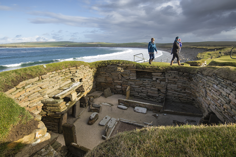 Visitors walking above one of the neolithic houses at Skara Brae