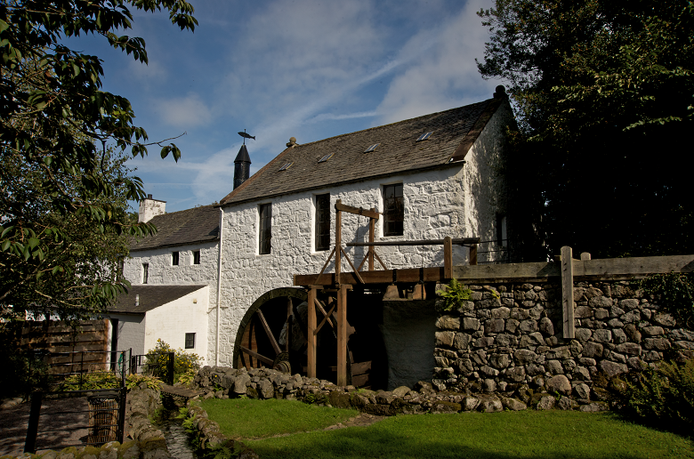 A traditional whitewashed mill building with a wooden waterwheel 