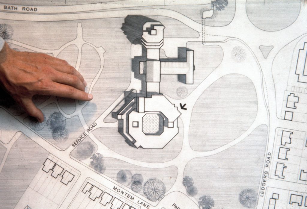 A hand rests on a 3D sketch of a building plan.