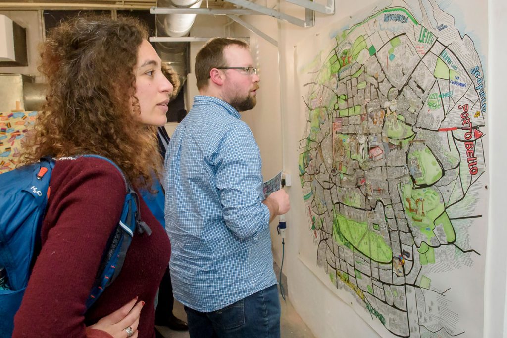 Two people looking at a large, artistically-drawn map of Edinburgh on a wall. 
