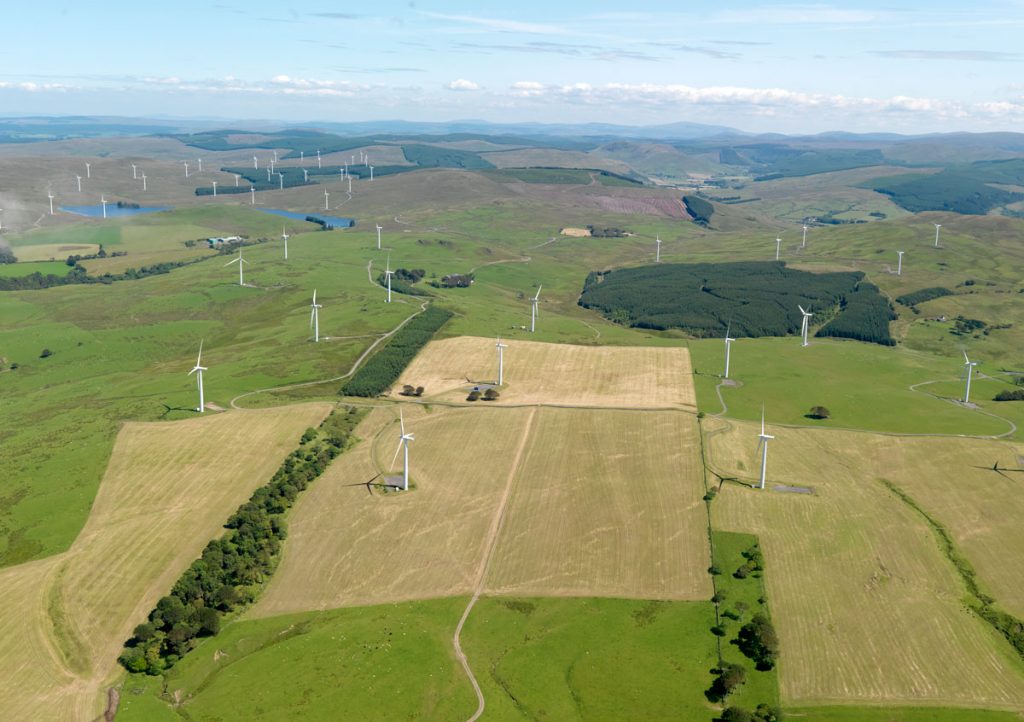 A bird's eye view over fields and a wind farm filled with turbines.