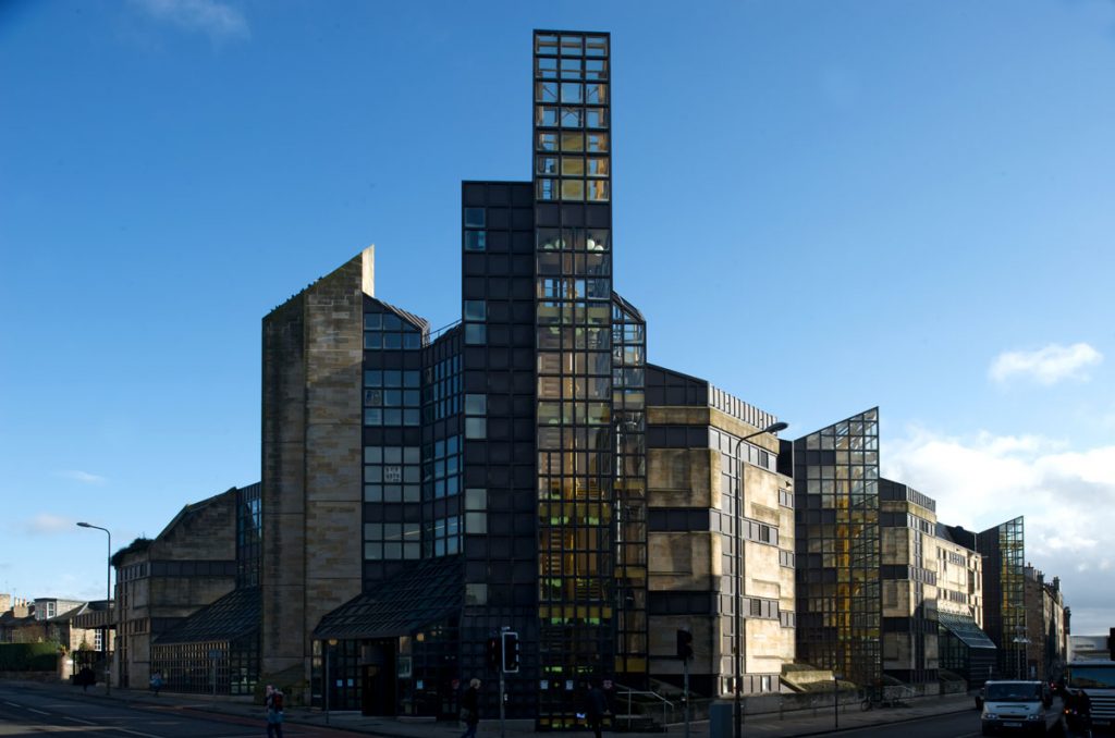 A building built of glass and blond sandstone on the corner of a junction.